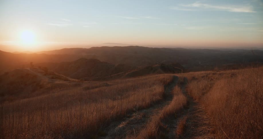 Landscape of country road leading down hill slope at sunset