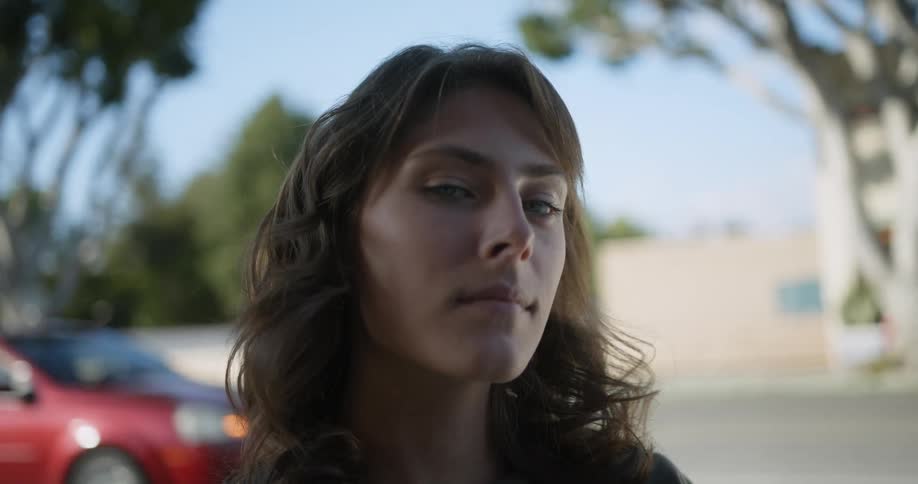 Woman with brown wavy hair and green eyes sits at table in front of cafe overlooking street
