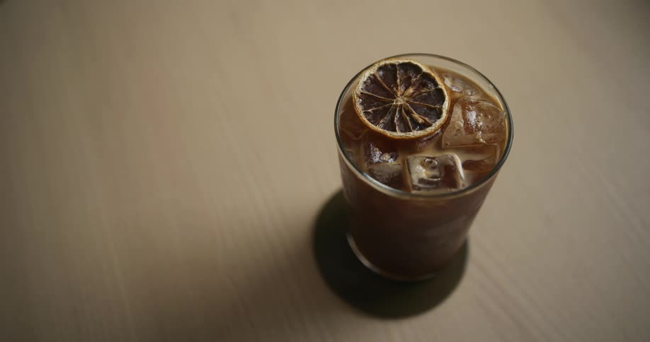 Person places iced drink decorated with sliced citrus on a coaster