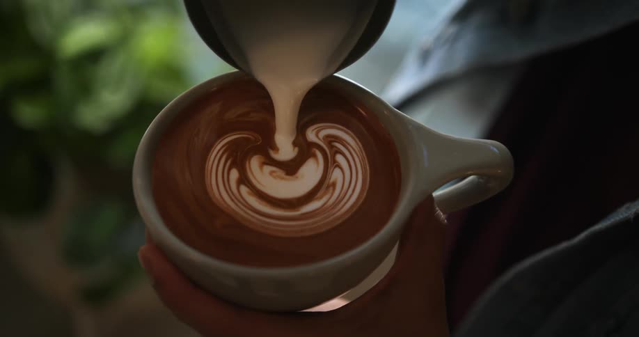 Barista creates foam art with milk on a cup of coffee