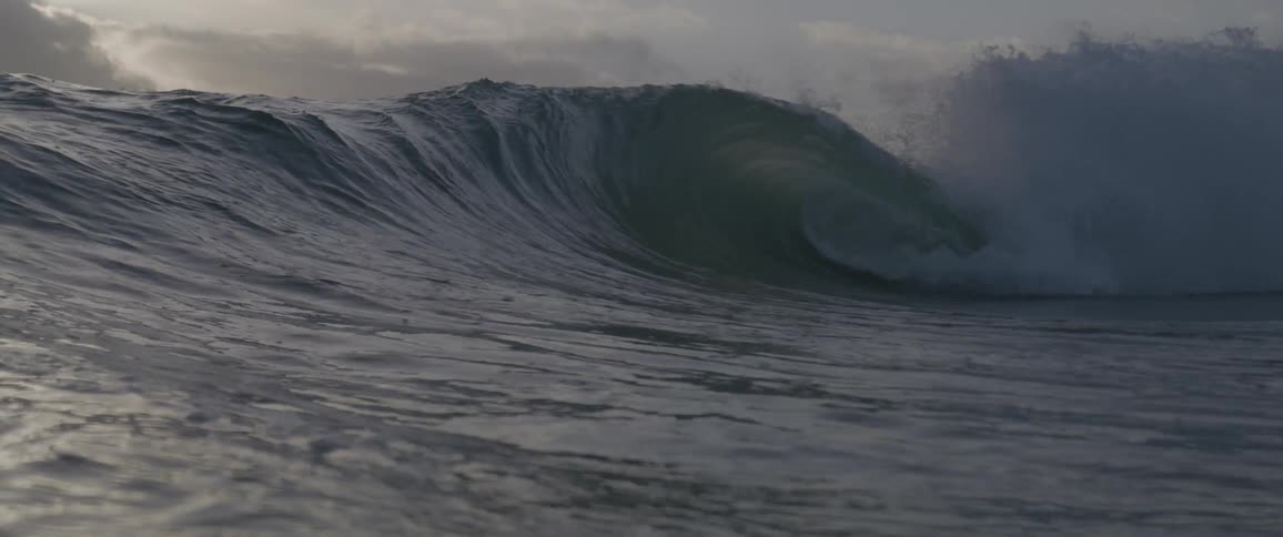 A big waves splashes as it rolls in under a cloudy sky