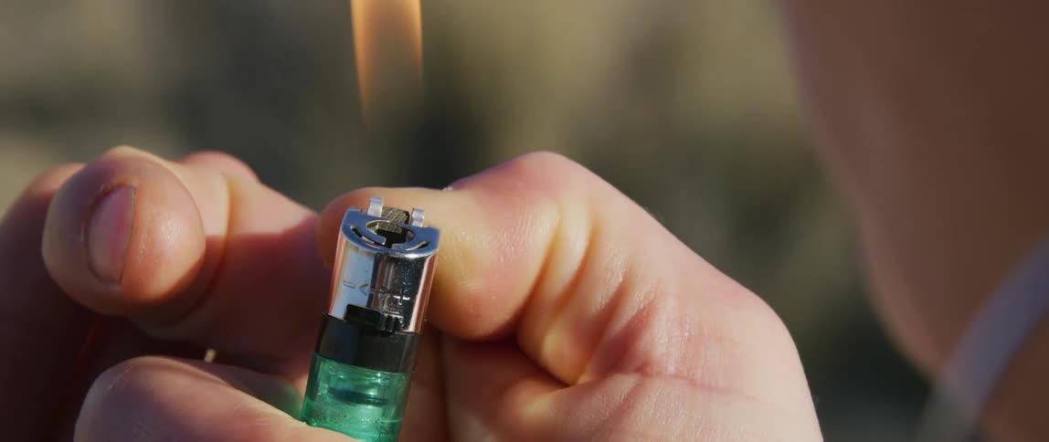 A person lighting the cigarette in their mouth with a lighter