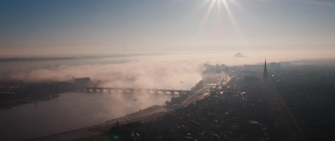 Sun sends rays down toward fog covered town and bridge spanned river