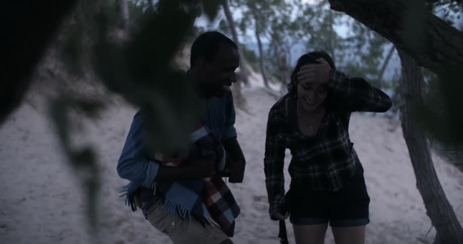 A man and a woman find shelter under a tree in a rainstorm