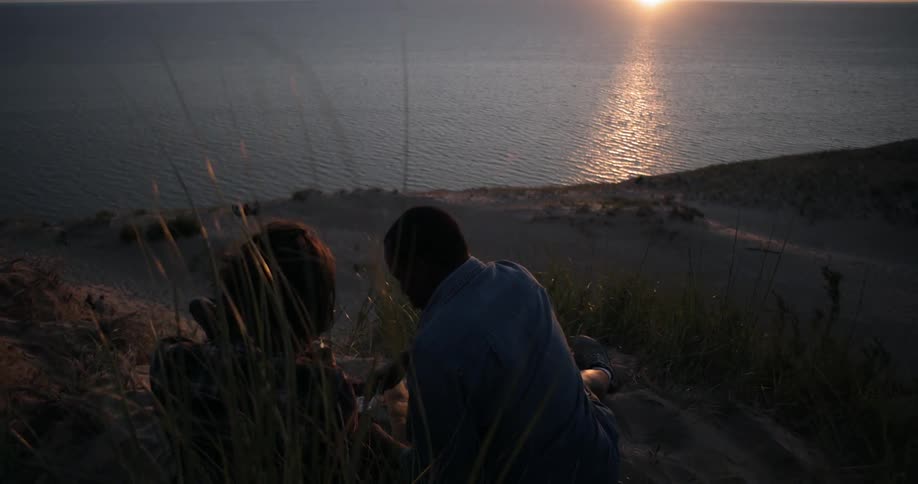 A man and woman sit on the beach at sunset