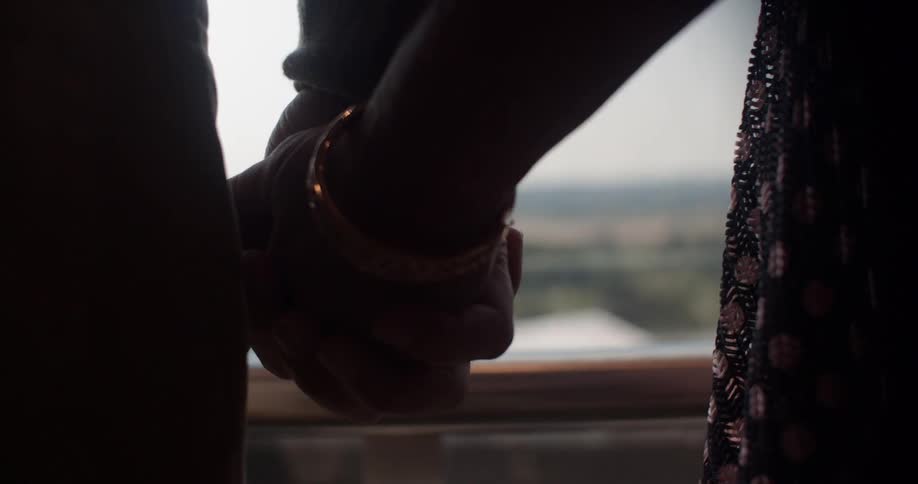 Two people hold hands while on a glass elevator in the day time