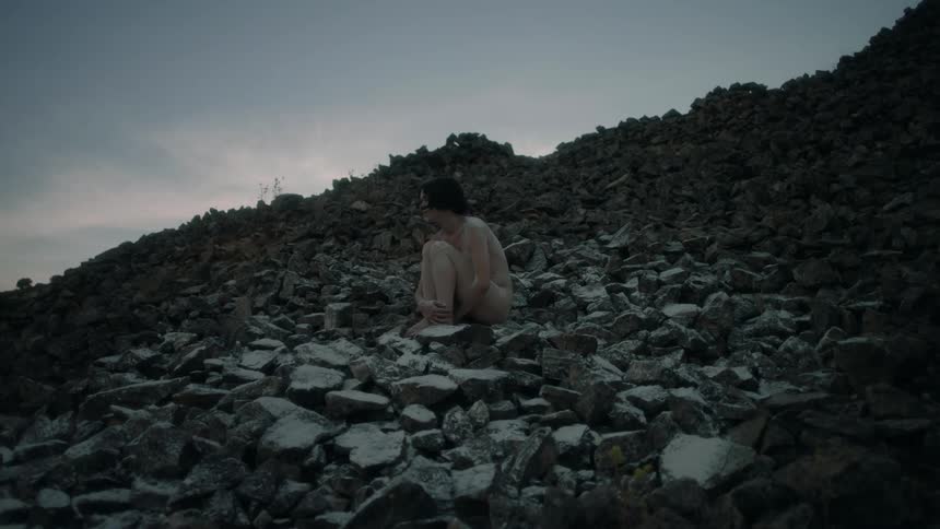 A sad person sitting on a lot of rocks outside