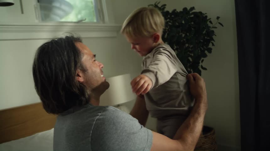 Father smiles while playing with his son in bedroom