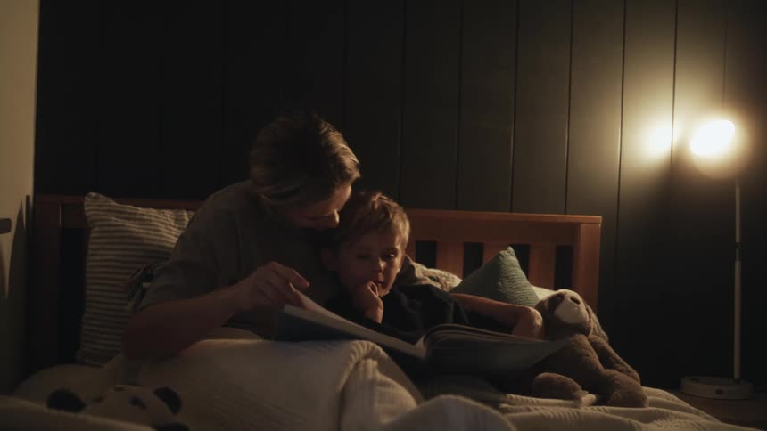 Mother reads to son sitting on bed in room