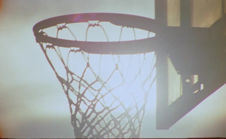 Sun glares down onto basketball hoop near tall building