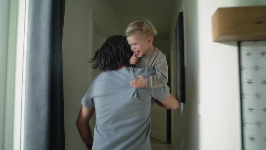 A father running room to room with his smiling son in his arms
