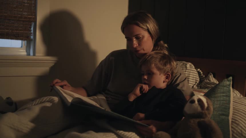 A woman is sitting in bed reading a book to her young son