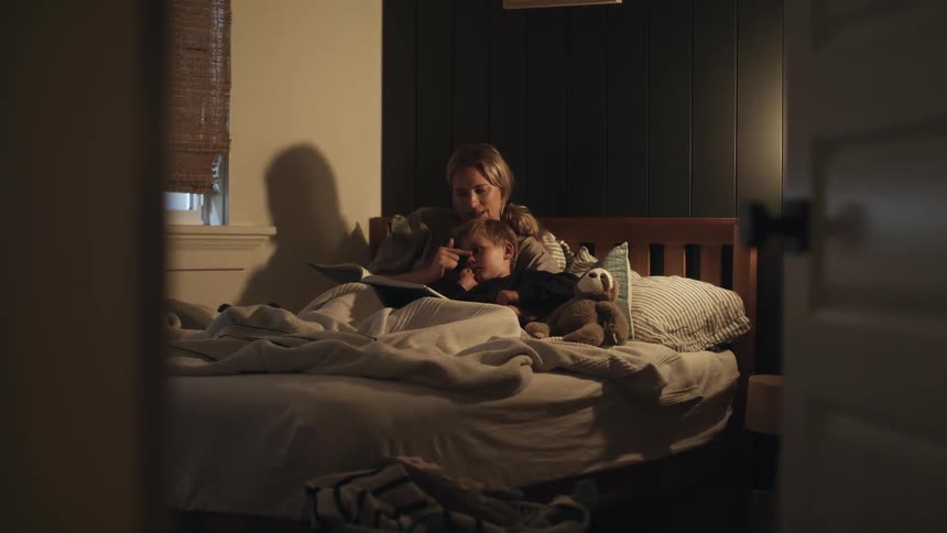 Mother sits in bed with son while reading him a book