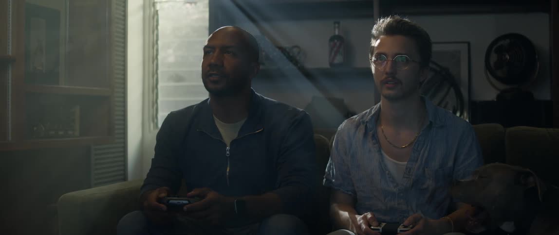 Two men sit on a couch and play a video game