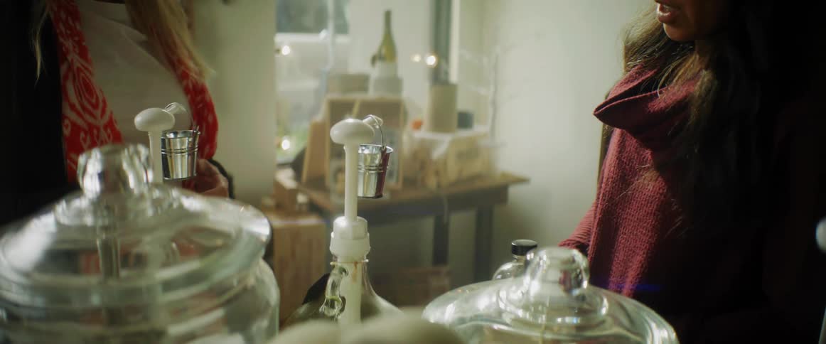 A woman places a top on a glass bottle while speaking to a woman in front of her