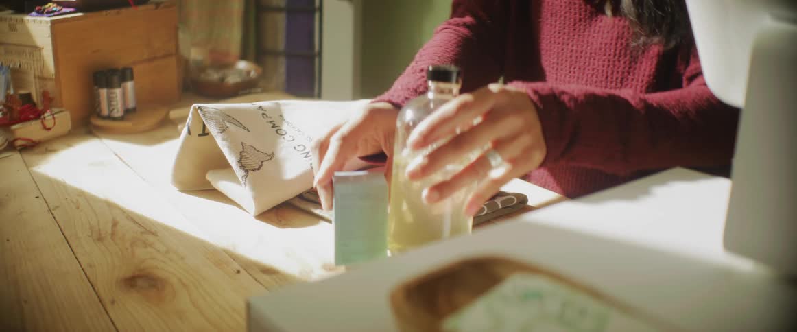 Woman with dark hair and crimson sweater sorts out her things on wooden table