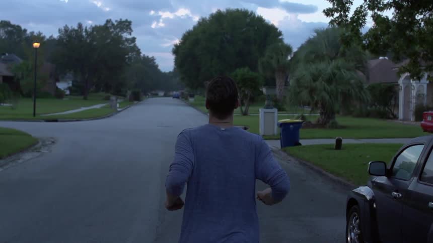 A man jogs in slow motion through a neighborhood at dawn