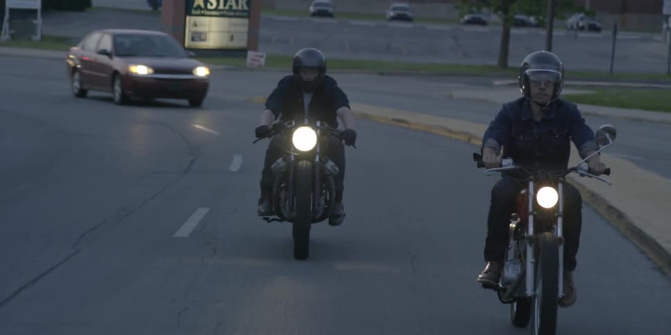 Motorcycles and cars drive down a road with their headlights on
