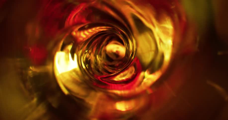 Top down close up of the interior of a blender spinning a spiral vortex of clear liquid under golden lights