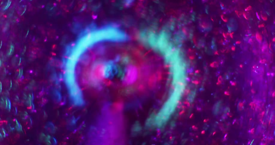 Red and purple particles rapidly move around a magenta vortex as blue light glows around the tunnel