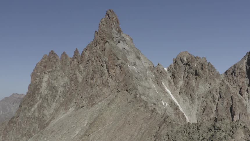 A mountain stands tall with a peak high in a clear sky and there are mountains in the distance