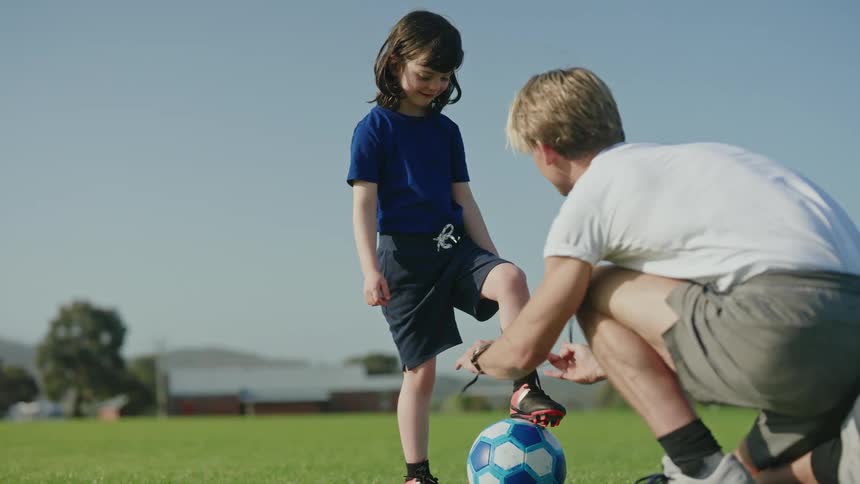 A father ties his sons sneaker on the soccer field