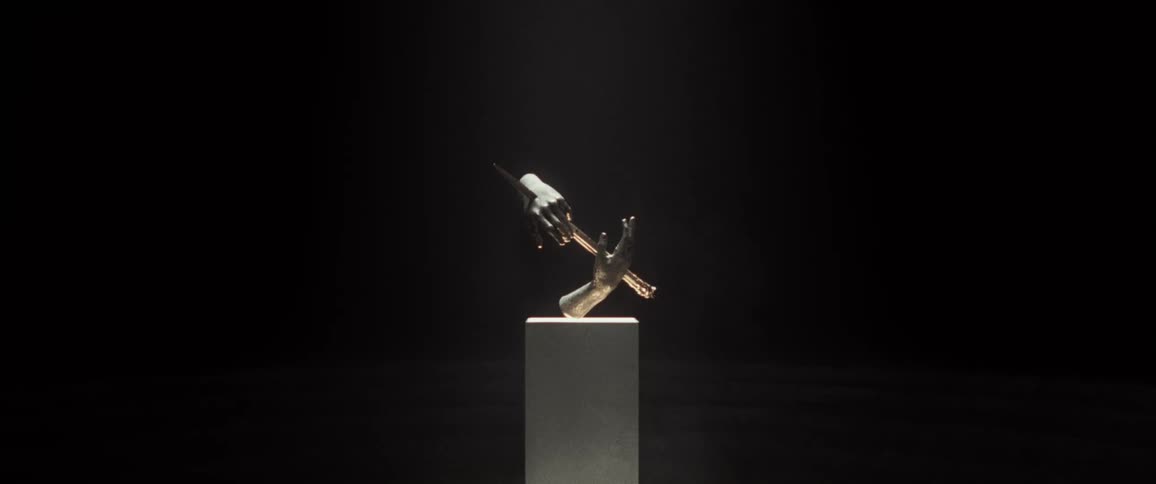Sculpture of hands pierced by blade sits on pedestal under spotlight in dark room
