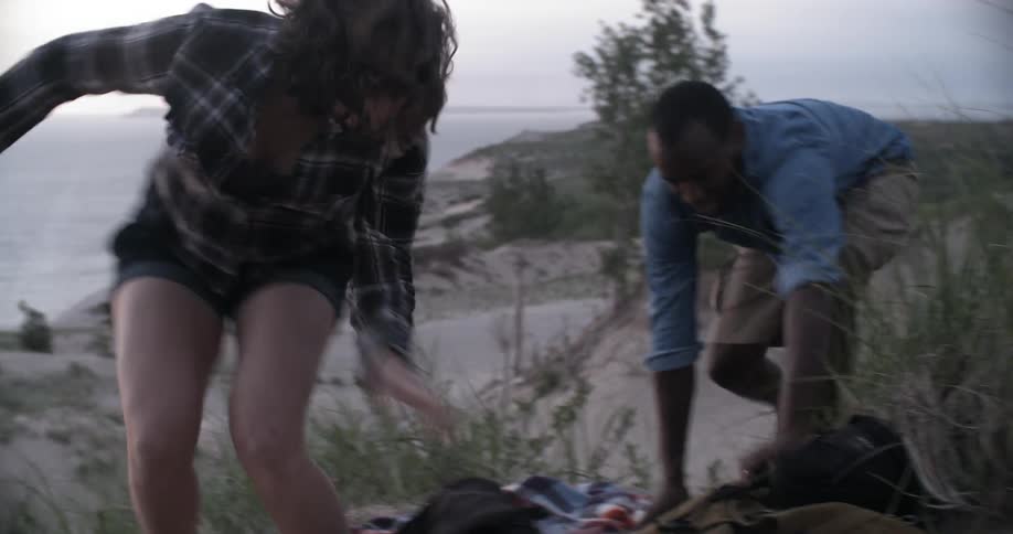 A man and woman quickly get up from laying in the sand and playfully run off