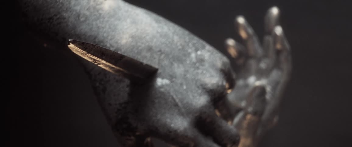 Light shines onto sculpture of two hands pierced by a blade