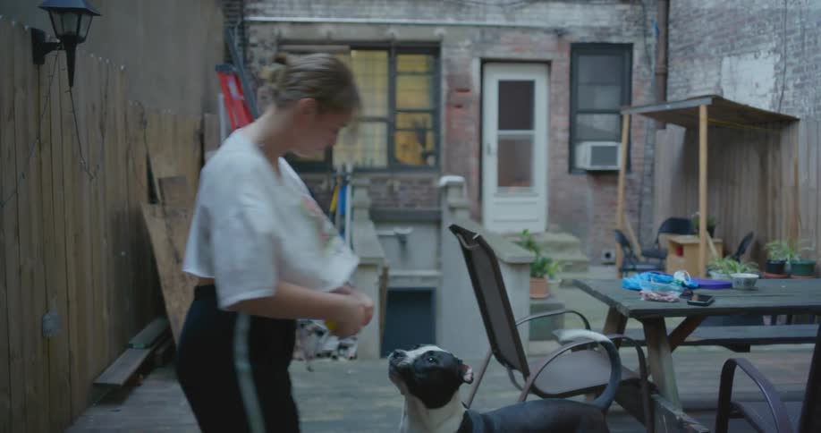 Blonde woman in white t shirt and black pants plays with dog in the backyard