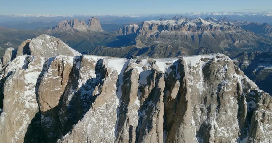 Sunlight shines on a building on top of a mountain ridge and there are mountains in the distance under a clear hazy sky