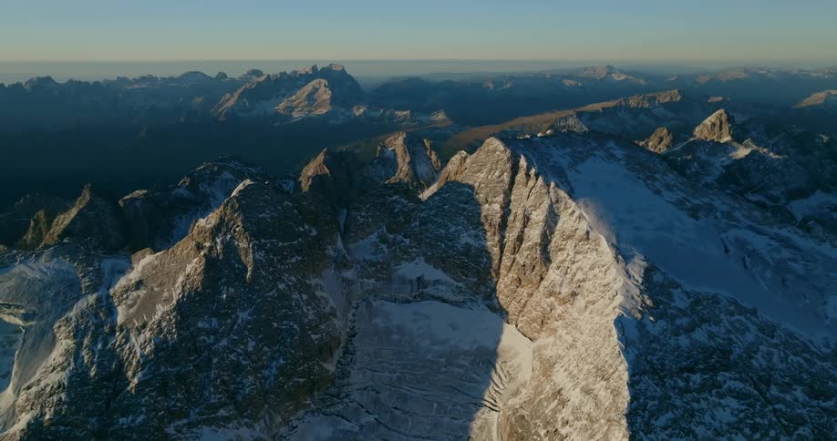 Snowy mountains stretching to the horizon on a misty day remain mostly in shadow