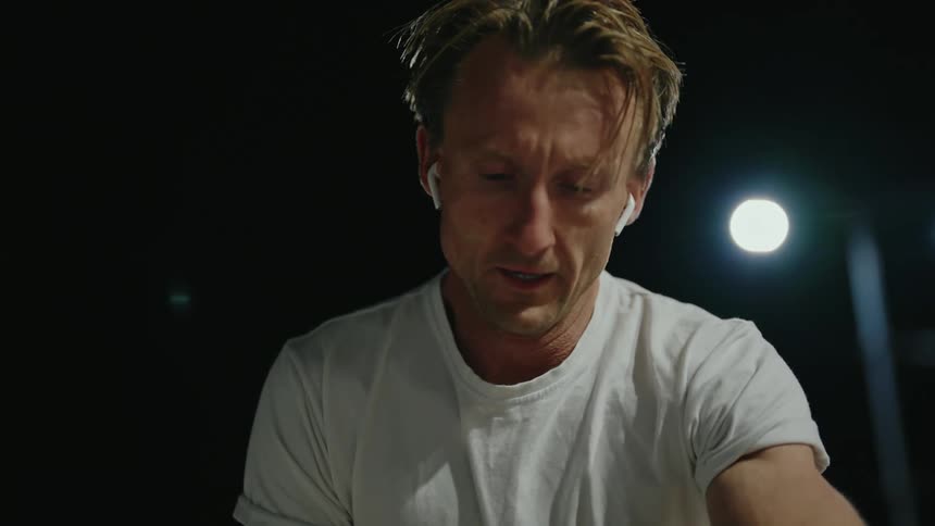 A man running outside at night stops and knees down and looks at his watch and then continues his run