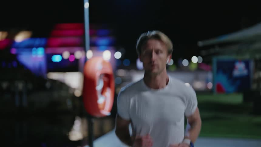 Blonde man wears earbuds as he runs along waterfront at night