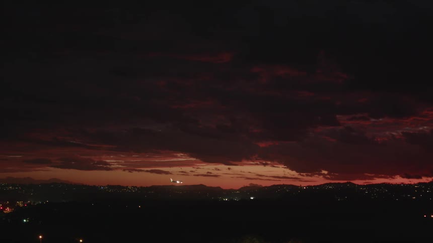 Airplane flies toward a landing at night through a red sky over city lights