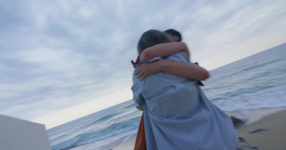 A woman walking through a tunnel towards the beach rushes to greet and hug her friend