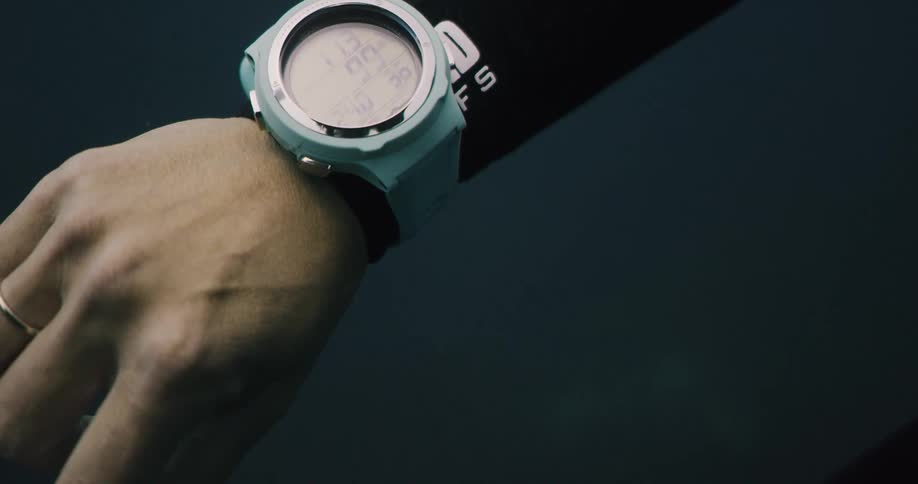 Female diver wearing wetsuit with red polished fingernails raises wrist with watch
