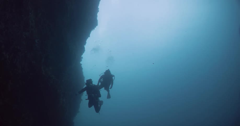 Two scuba divers swim around the rocks