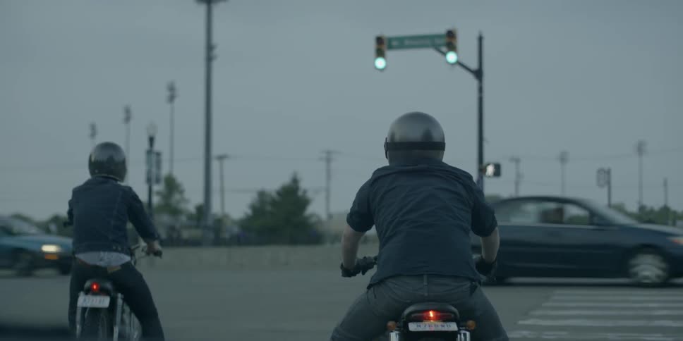 Two people on motorcycles wait at a red light