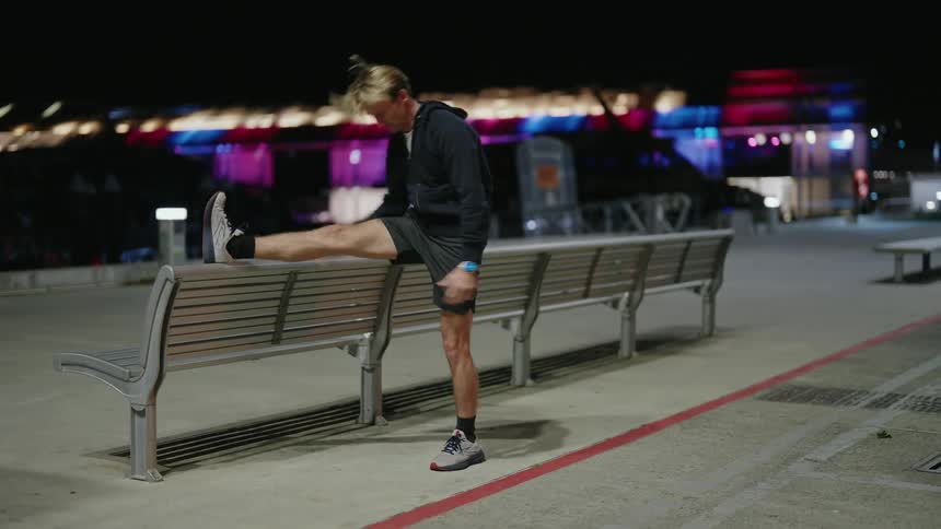 Man stretches on a bench on a park in the city at night