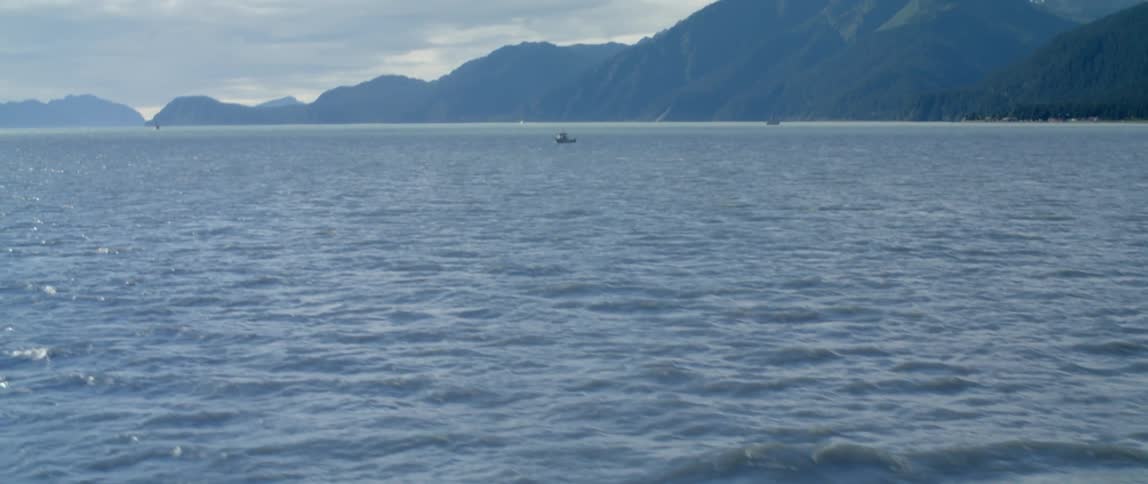 Boats float on the water close to mountains on shore on foggy day under a cloudy sky