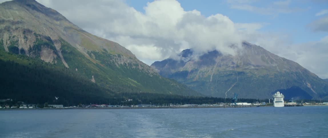Birds flying over a lake with a large boat in it in front of hills