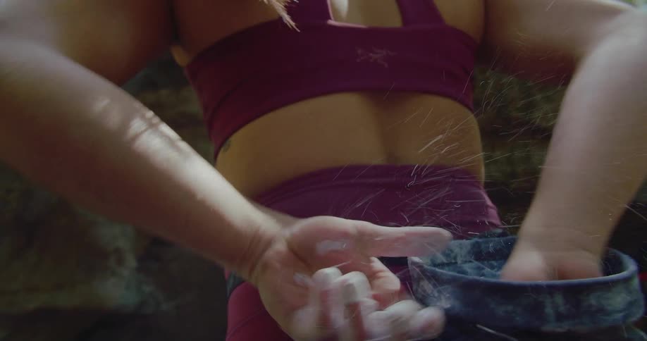 A rock climber chalks up her hands behind her back from a bag around her waist