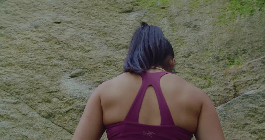 A woman reaches into a pouch on her belt to chalk her hands before beginning to climb a rock face