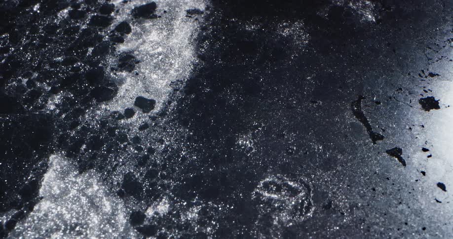 Water sparkles as it flows through dark gray ice sheet