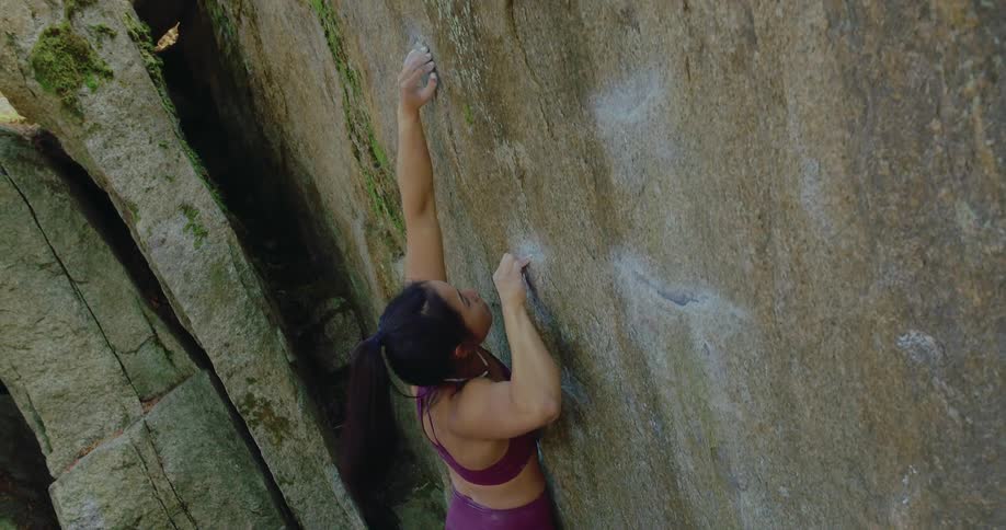 A woman climbs up a steep mountain wall using handles