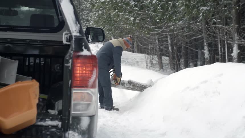 A man cuts a fallen tree with a chainsaw on a snowy winter day