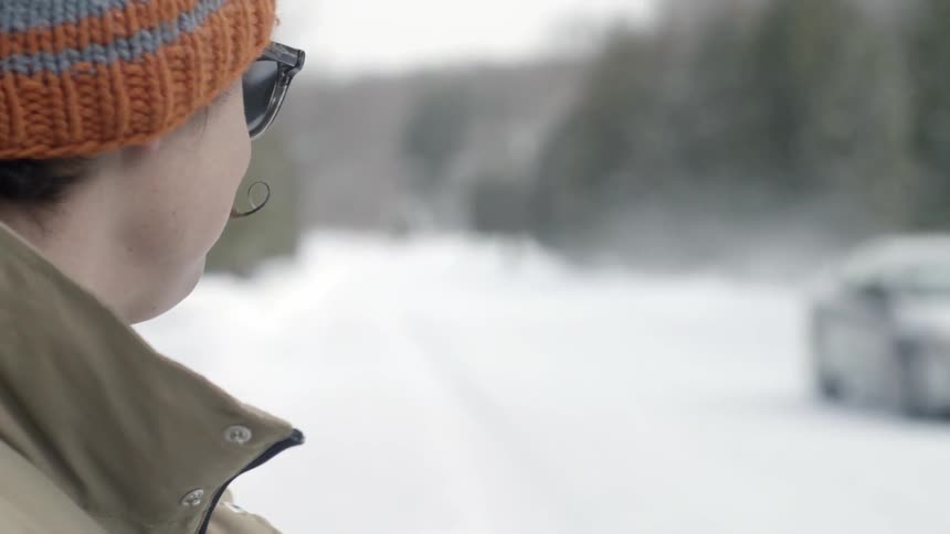A man waves as a car drives by in the snow