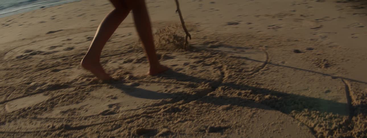 A young girl is etching large circles on a beach in the evening
