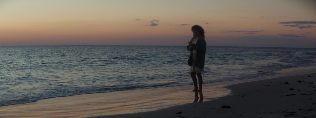 A young woman stands on the beach as the sun sets